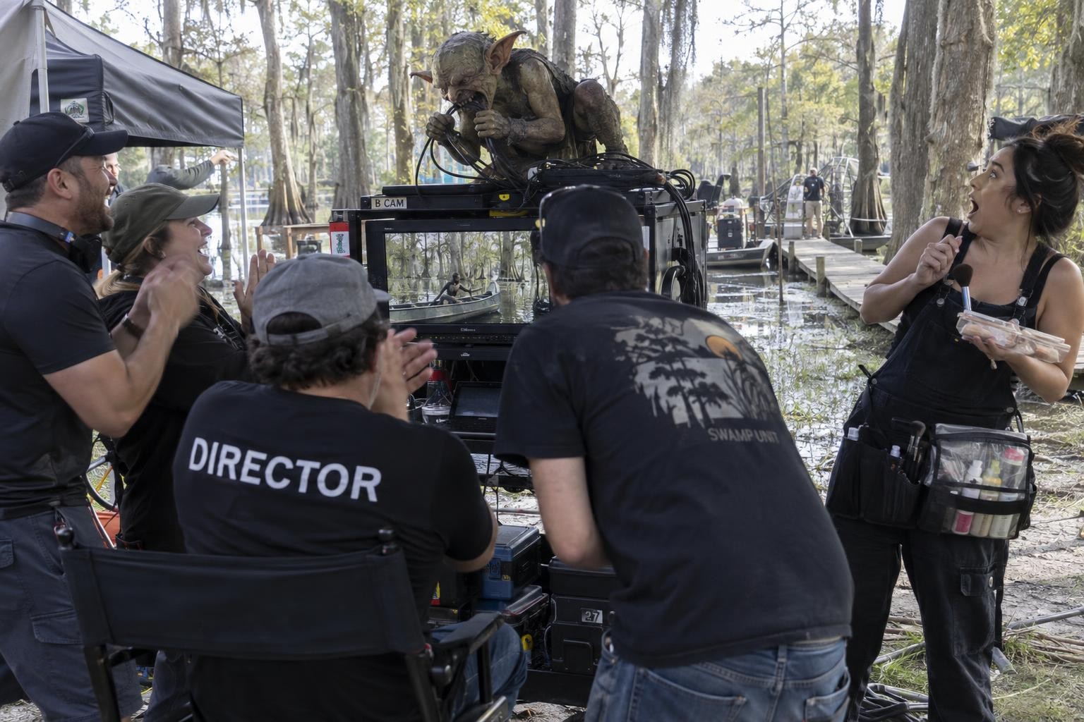 A muddy goblin chews on cables atop a video cart while a terrified makeup artist watches the oblivious, laughing crew.