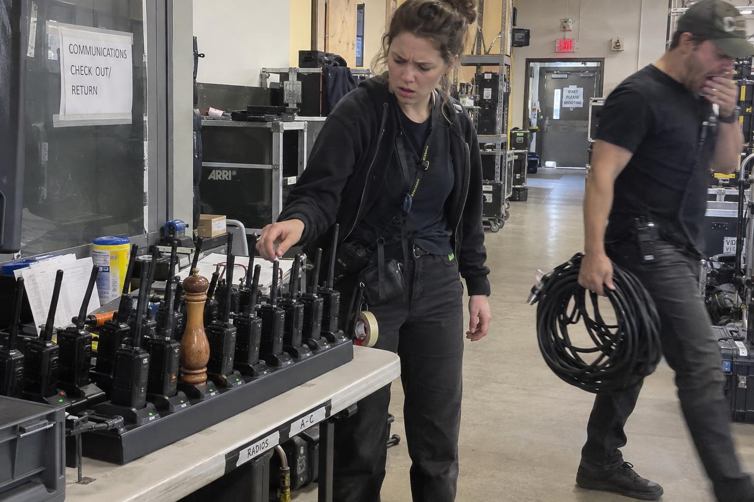 A confused production assistant finds a tall wooden pepper grinder sitting in a walkie-talkie charging station.
