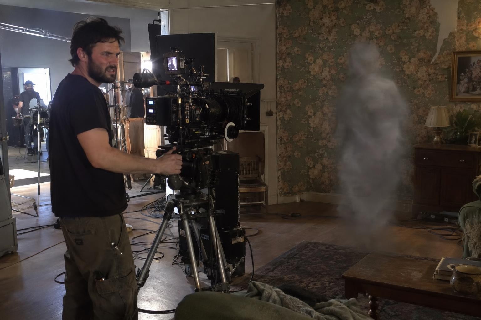 A frustrated camera assistant at a cinema camera looks at a blurry, smoky ghost floating just in front of the lens.